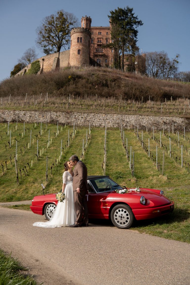 Brautpaar posiert mit dem Oldtimer vor dem Schloss Ortenberg